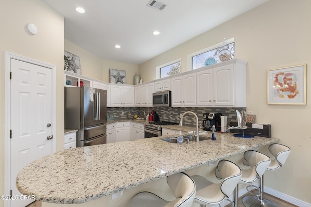 kitchen with visible vents, a breakfast bar, a sink, appliances with stainless steel finishes, and a peninsula