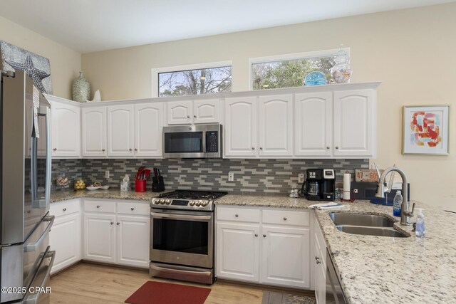 kitchen featuring decorative backsplash, white cabinets, stainless steel appliances, and a sink