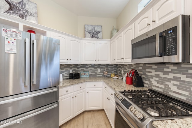 kitchen with light wood finished floors, light stone countertops, decorative backsplash, appliances with stainless steel finishes, and white cabinetry