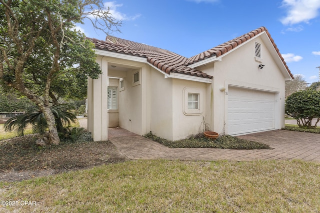 view of front of property featuring stucco siding, a tiled roof, decorative driveway, and a garage