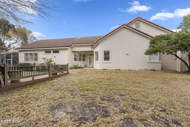 back of house featuring a tile roof, stucco siding, glass enclosure, a deck, and a yard