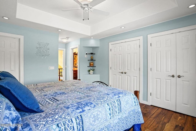 bedroom featuring a tray ceiling, dark wood-style flooring, recessed lighting, and two closets