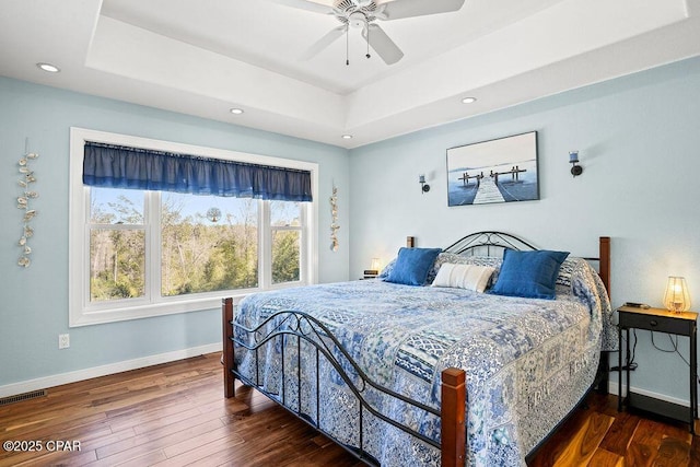 bedroom with hardwood / wood-style flooring, a raised ceiling, visible vents, and baseboards