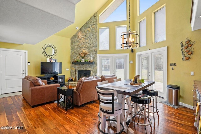 dining space with baseboards, french doors, dark wood-type flooring, a stone fireplace, and a chandelier