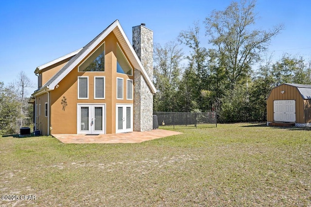 rear view of house with fence, a yard, french doors, a storage unit, and a patio area