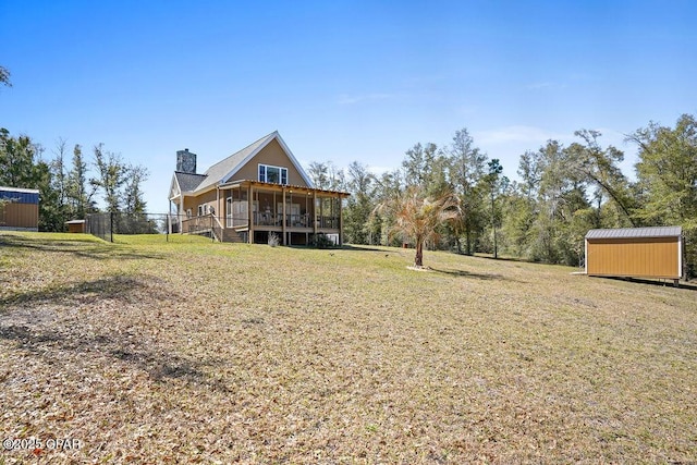 back of property featuring an outbuilding, a sunroom, a lawn, a storage unit, and a chimney