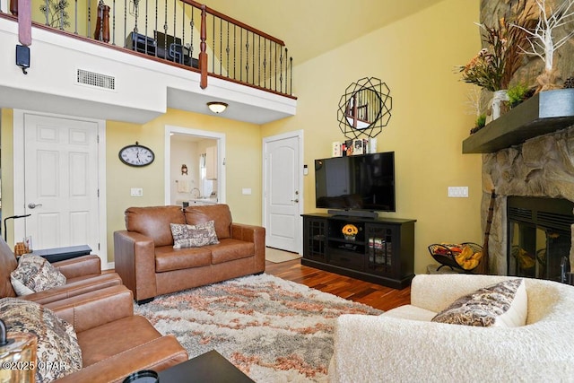 living room featuring a stone fireplace, a high ceiling, wood finished floors, and visible vents