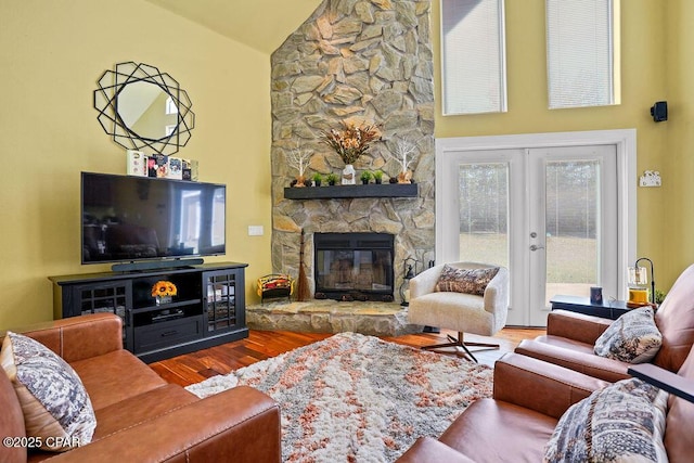 living area with high vaulted ceiling, french doors, a stone fireplace, and wood finished floors