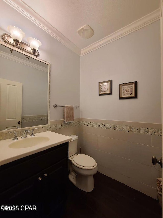 bathroom featuring tile walls, crown molding, toilet, vanity, and wainscoting