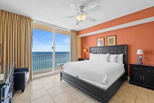 bedroom featuring access to exterior, a water view, a ceiling fan, light tile patterned flooring, and a wall of windows