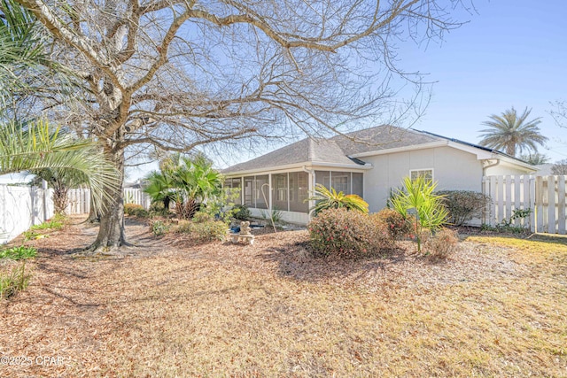 view of property exterior featuring a shingled roof, a fenced backyard, and a sunroom