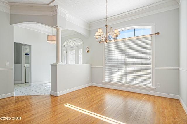 spare room with arched walkways, hardwood / wood-style flooring, an inviting chandelier, crown molding, and ornate columns