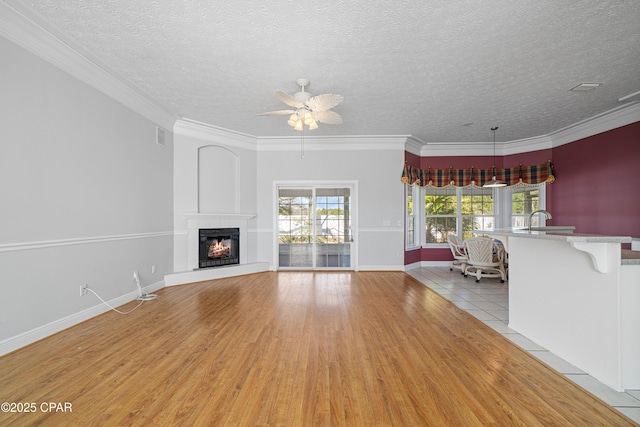 unfurnished living room featuring a textured ceiling, ceiling fan, light wood-style floors, ornamental molding, and a glass covered fireplace