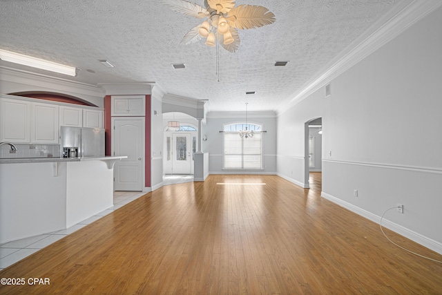 unfurnished living room featuring visible vents, arched walkways, ornamental molding, light wood-style floors, and ceiling fan with notable chandelier