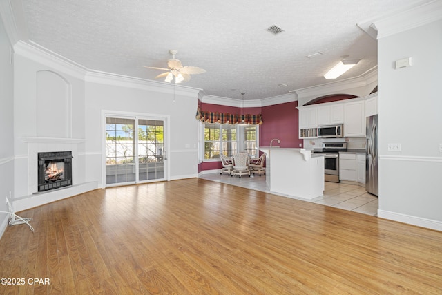 unfurnished living room with a lit fireplace, ornamental molding, visible vents, and light wood-style floors