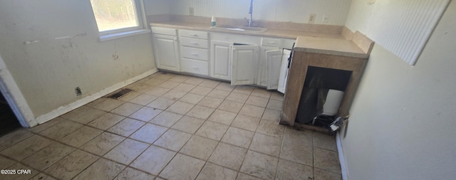 kitchen featuring visible vents, baseboards, a sink, light countertops, and white cabinetry