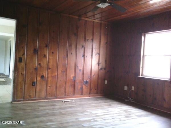 unfurnished room featuring wooden ceiling, wooden walls, wood finished floors, a ceiling fan, and visible vents