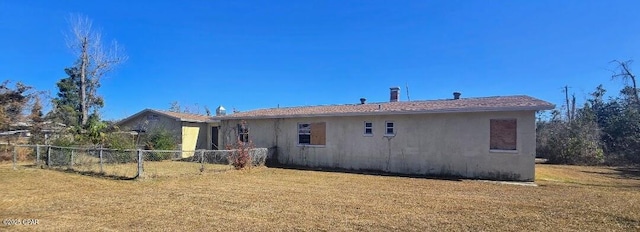 rear view of house featuring stucco siding, a lawn, and fence