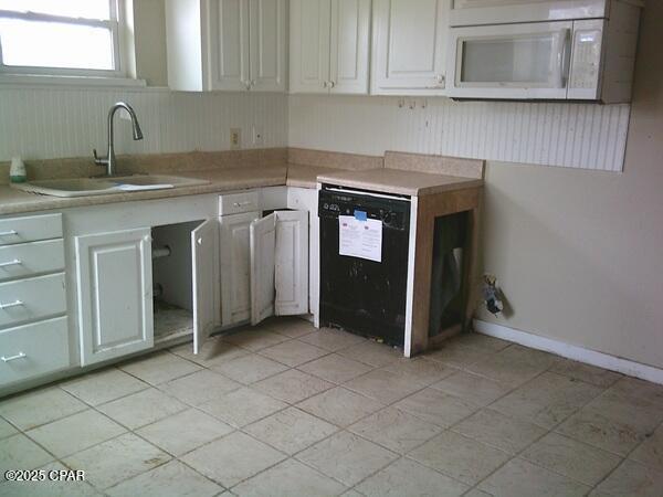 kitchen with white microwave, light countertops, black dishwasher, and a sink