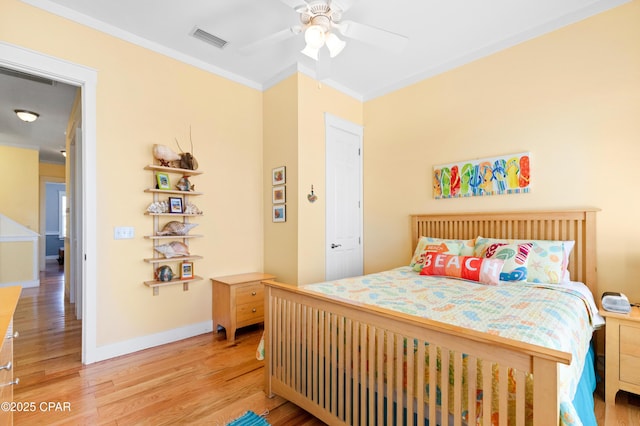 bedroom featuring ceiling fan, light wood-style flooring, visible vents, baseboards, and crown molding