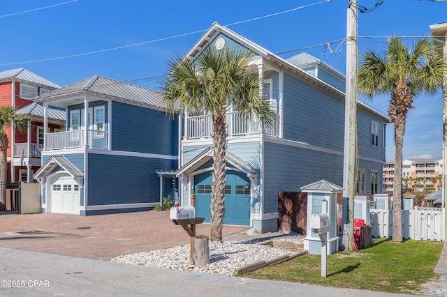 view of front of house with a balcony, metal roof, an attached garage, fence, and decorative driveway