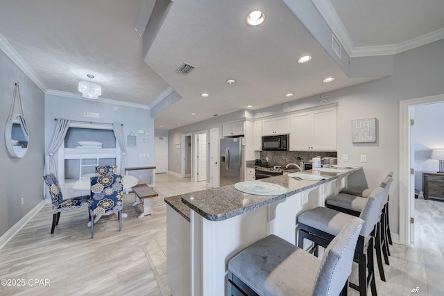 kitchen with a breakfast bar, ornamental molding, decorative backsplash, appliances with stainless steel finishes, and white cabinetry