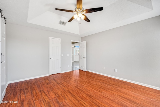 unfurnished bedroom featuring a raised ceiling, visible vents, ceiling fan, wood finished floors, and baseboards