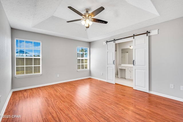 unfurnished bedroom with a barn door, baseboards, a tray ceiling, a textured ceiling, and light wood-type flooring