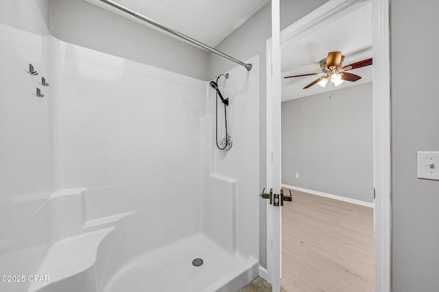 bathroom featuring a ceiling fan, a shower stall, baseboards, and wood finished floors