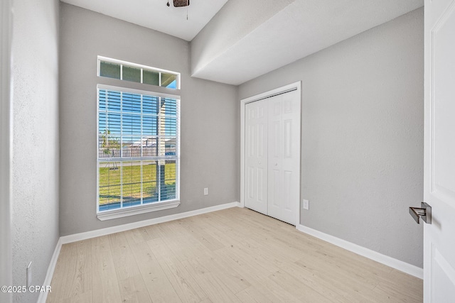 unfurnished bedroom with a textured wall, a closet, wood finished floors, and baseboards