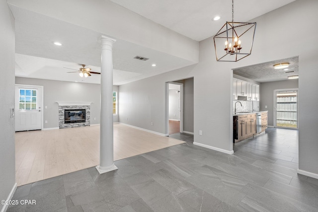 unfurnished living room with decorative columns, visible vents, a ceiling fan, a sink, and a stone fireplace