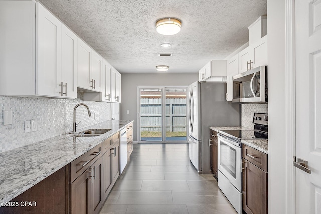 kitchen featuring visible vents, light stone counters, stainless steel appliances, white cabinetry, and a sink