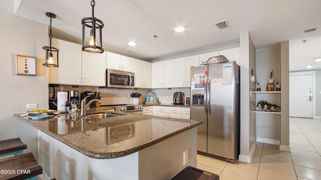 kitchen with stainless steel appliances, visible vents, a sink, dark stone counters, and a peninsula