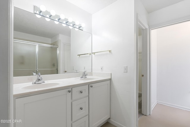 full bath with double vanity, a shower stall, baseboards, and a sink