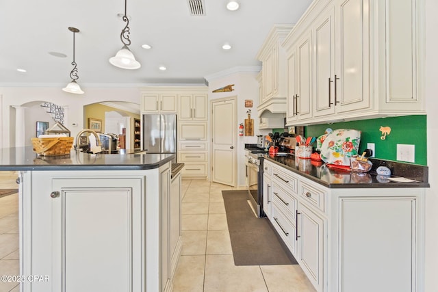 kitchen with an island with sink, ornamental molding, dark countertops, appliances with stainless steel finishes, and light tile patterned floors