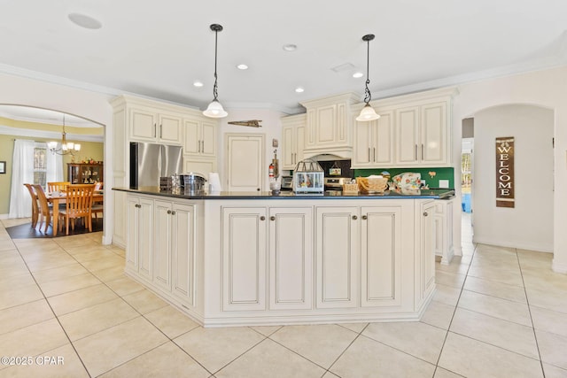 kitchen featuring arched walkways, cream cabinetry, dark countertops, and freestanding refrigerator