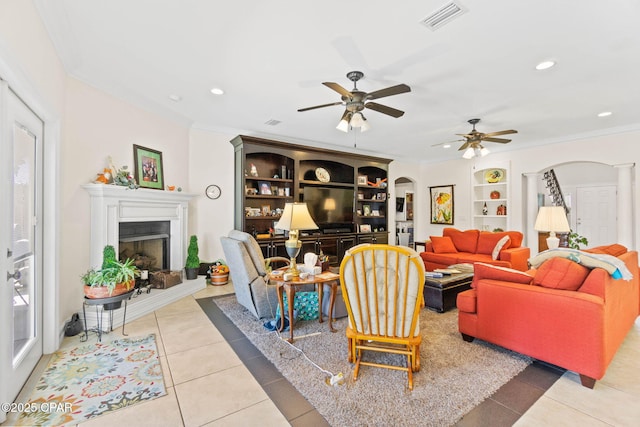 tiled living area with visible vents, recessed lighting, arched walkways, a fireplace with raised hearth, and crown molding