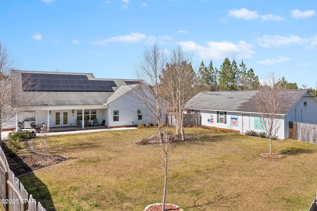 back of property with roof mounted solar panels, a fenced backyard, french doors, a yard, and a patio area