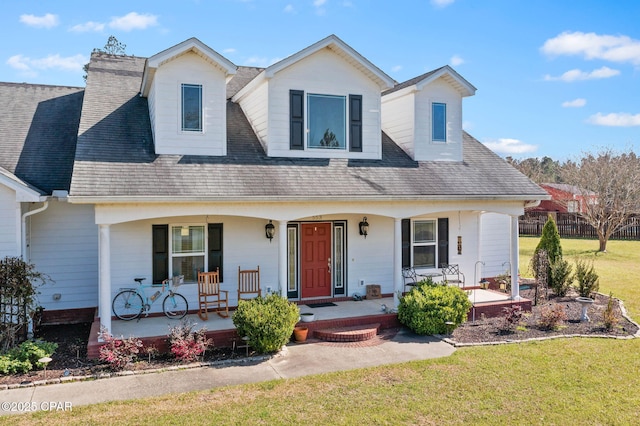 view of front of home with a porch, a shingled roof, a front lawn, and fence