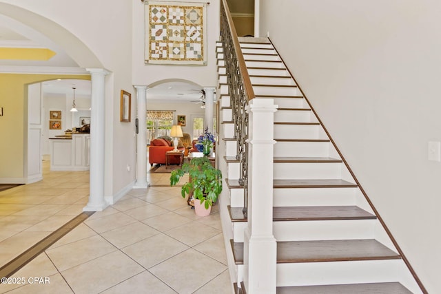 staircase with baseboards, decorative columns, arched walkways, crown molding, and tile patterned floors