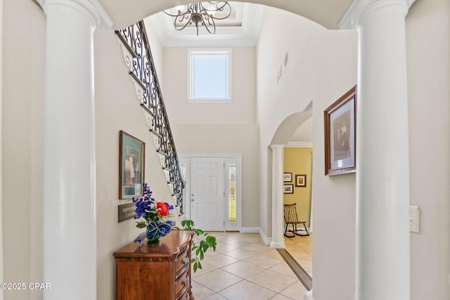 foyer featuring arched walkways, a high ceiling, crown molding, light tile patterned floors, and ornate columns