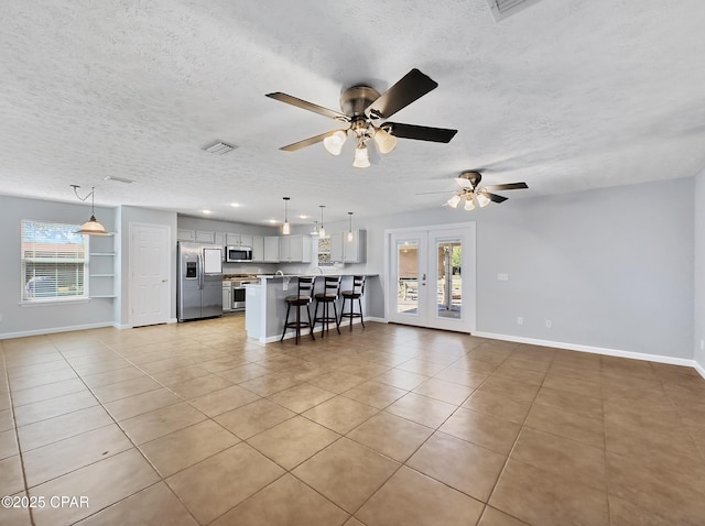 unfurnished living room featuring baseboards, visible vents, a wealth of natural light, and a textured ceiling