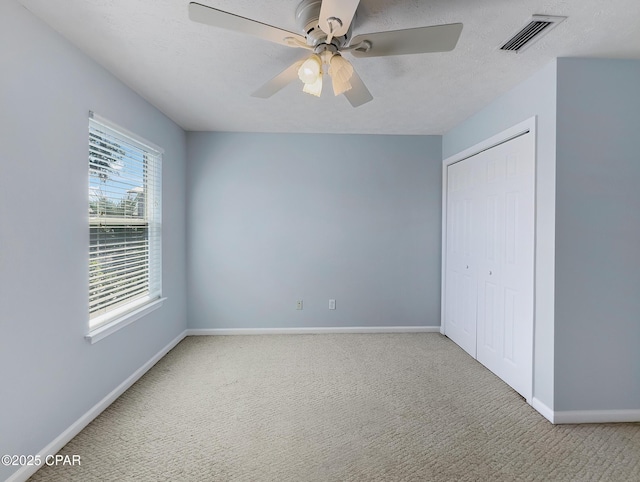 unfurnished bedroom with visible vents, a textured ceiling, a closet, carpet flooring, and baseboards