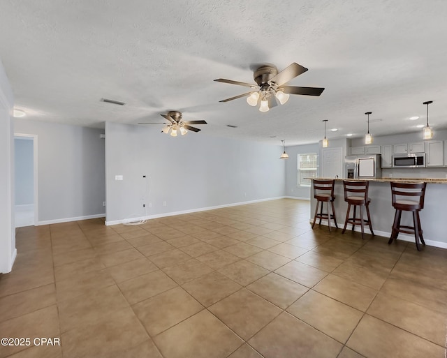 unfurnished living room with light tile patterned floors, a ceiling fan, baseboards, visible vents, and a textured ceiling