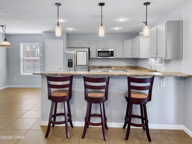 kitchen with light stone counters, light tile patterned floors, appliances with stainless steel finishes, and a peninsula