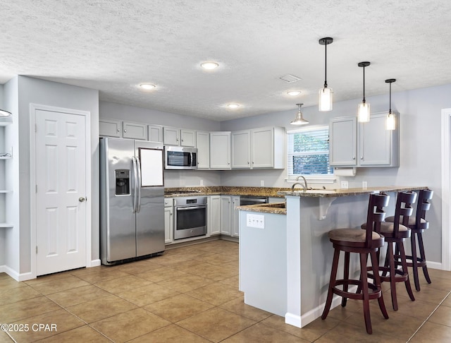 kitchen featuring visible vents, a peninsula, a kitchen breakfast bar, appliances with stainless steel finishes, and decorative light fixtures