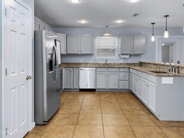 kitchen with dark stone countertops, a peninsula, light tile patterned flooring, a sink, and appliances with stainless steel finishes