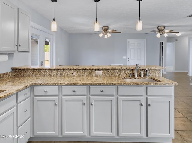 kitchen with a sink, decorative light fixtures, light tile patterned floors, and white cabinetry