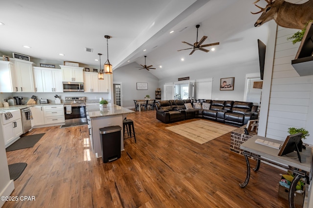 kitchen with open floor plan, wood-type flooring, appliances with stainless steel finishes, white cabinets, and light stone countertops