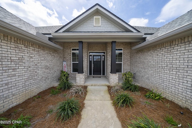 doorway to property with roof with shingles, a porch, and brick siding